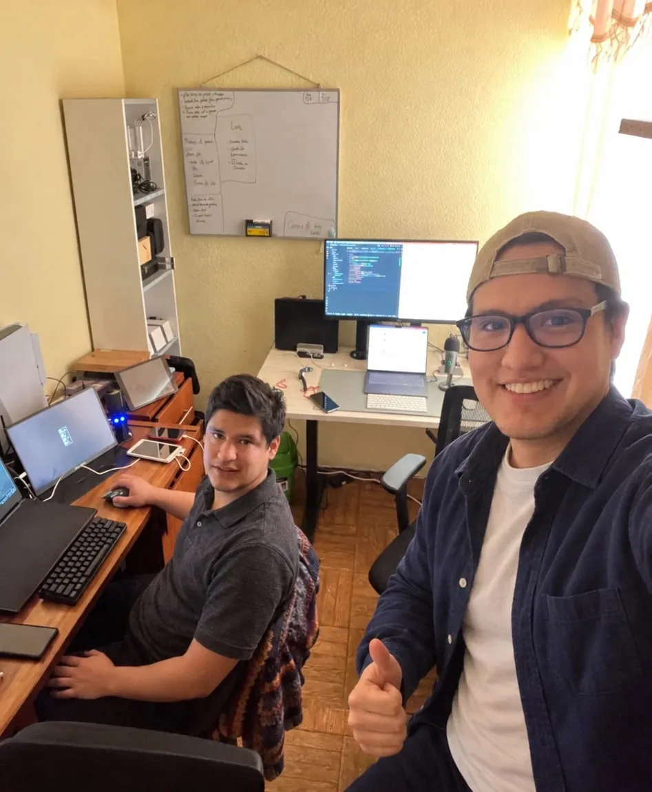 Two members of the Wasilabs team in their Lima workspace, at their computers in front of a whiteboard with sketches.